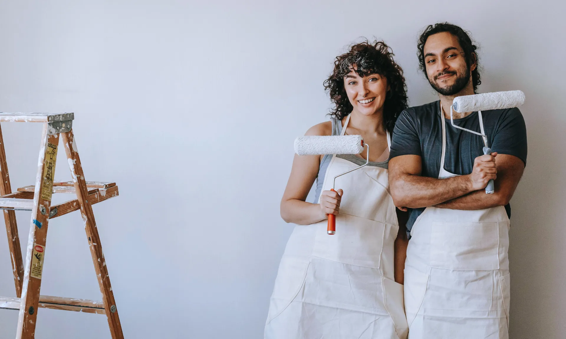 DIY home decor ideas for beginners featuring two people holding paint rollers while preparing to paint a room for a budget-friendly home makeover