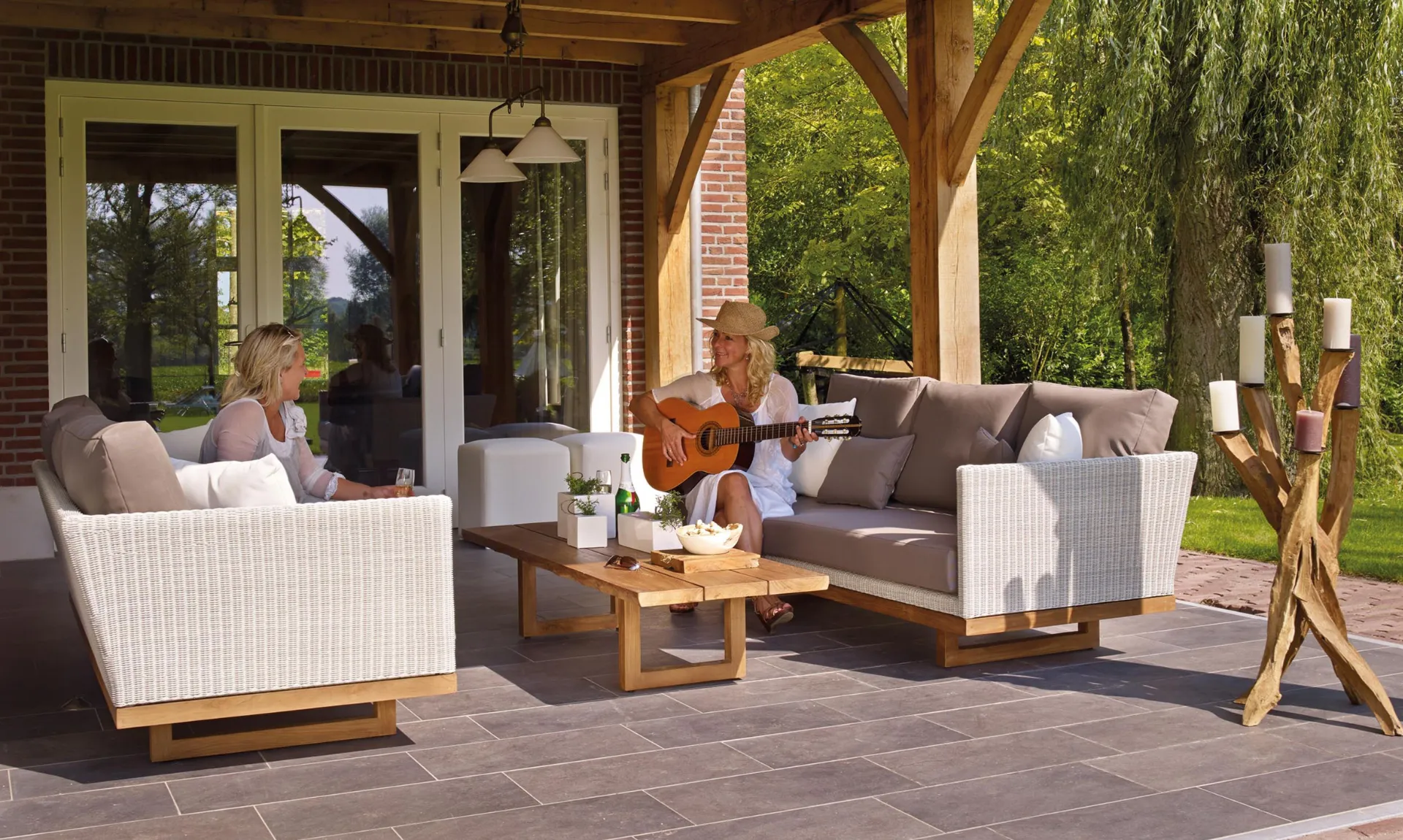 Covered patio with wicker outdoor furniture, neutral cushions, a wooden coffee table, and a cozy seating area overlooking a lush garden.
