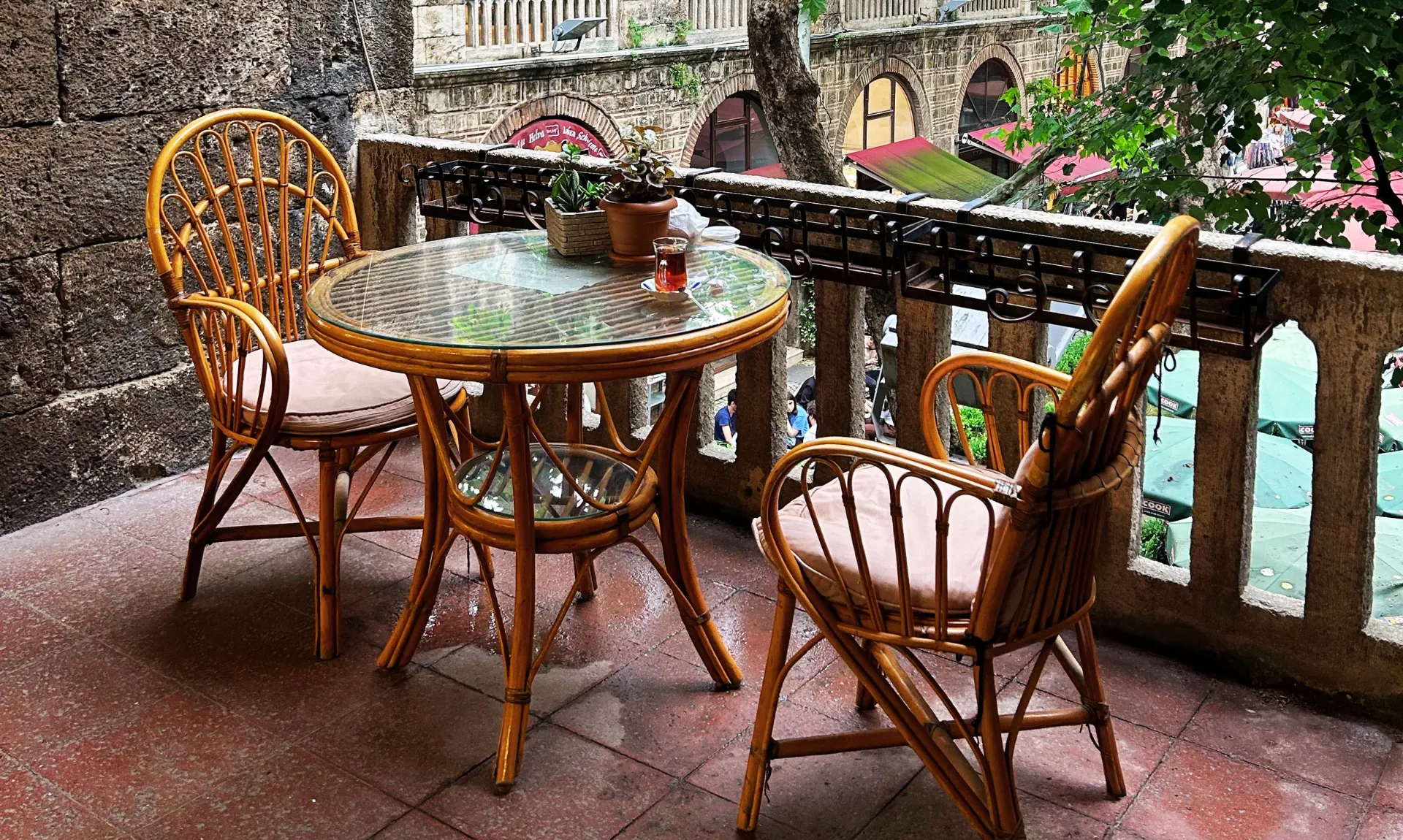 Cozy patio with rattan chairs, a round glass table, potted plants, and a relaxing outdoor seating area overlooking a courtyard.